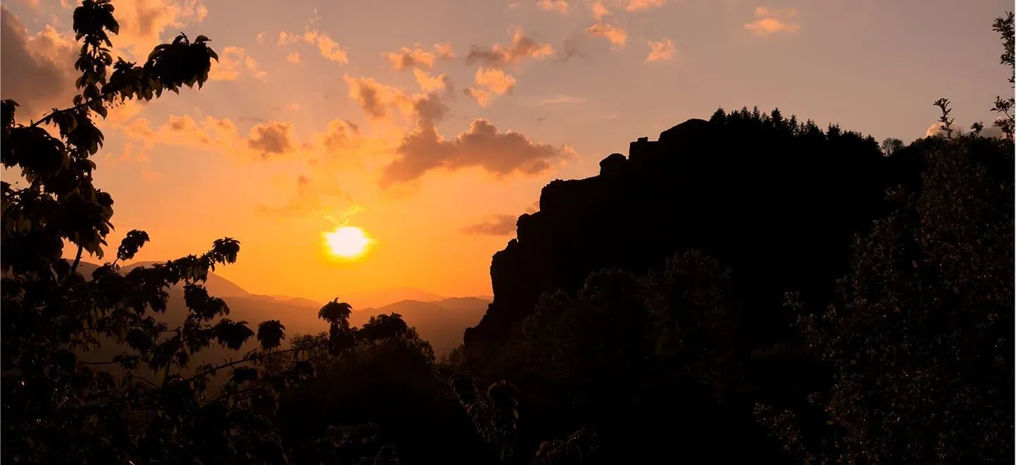 Il Gigante di Duronia al tramonto, con la caratteristica formazione rocciosa in silhouette sul paesaggio montano e il sole che illumina il cielo di tonalità arancioni.