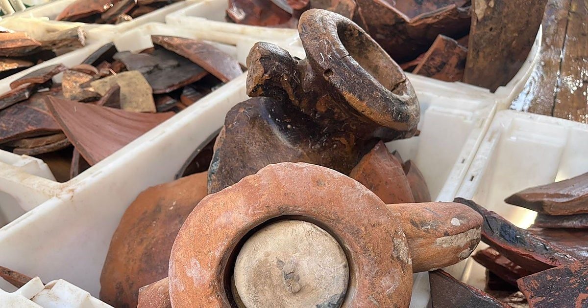 Primo piano di reperti archeologici in terracotta e ceramica, tra cui grandi frammenti e oggetti circolari, raccolti all’interno di contenitori bianchi.