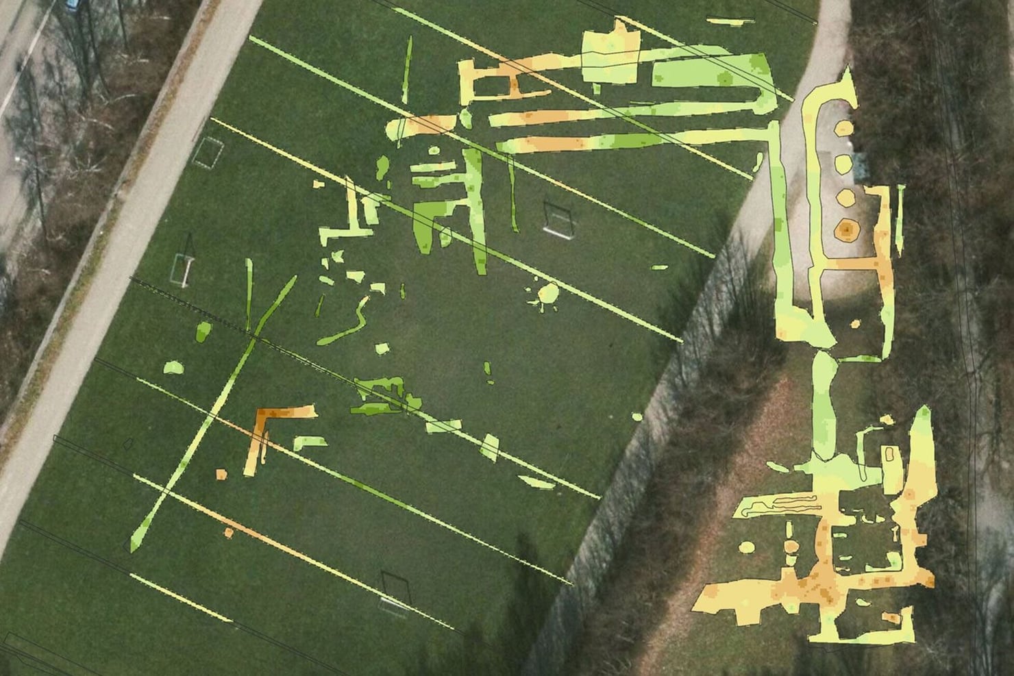 Veduta aerea di un’area verde attraversata da strade e circondata da zone alberate. Sull’immagine sono sovrapposte in verde, giallo e arancione le tracce di strutture e altri elementi individuati nel sottosuolo, distribuiti in diverse parti del terreno.