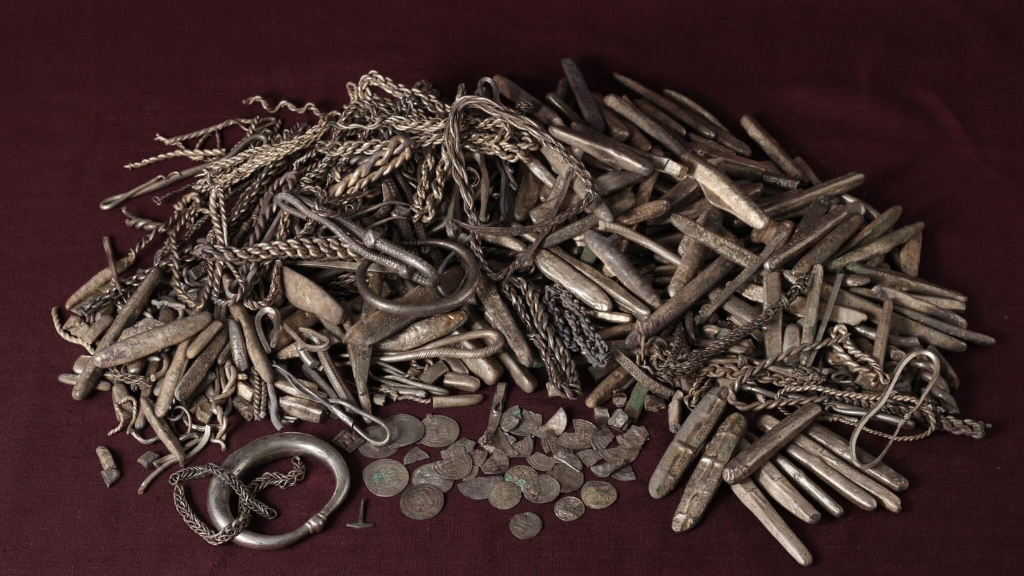 Primo piano di oggetti metallici provenienti da un tesoro vichingo, su una superficie uniforme.