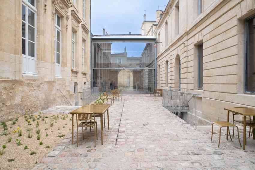 Vista del cortile posteriore, con il padiglione che collega l’hôtel particulier all’antica prigione. Arredi per esterni di Pauline Deltour, collezione “Patio”.