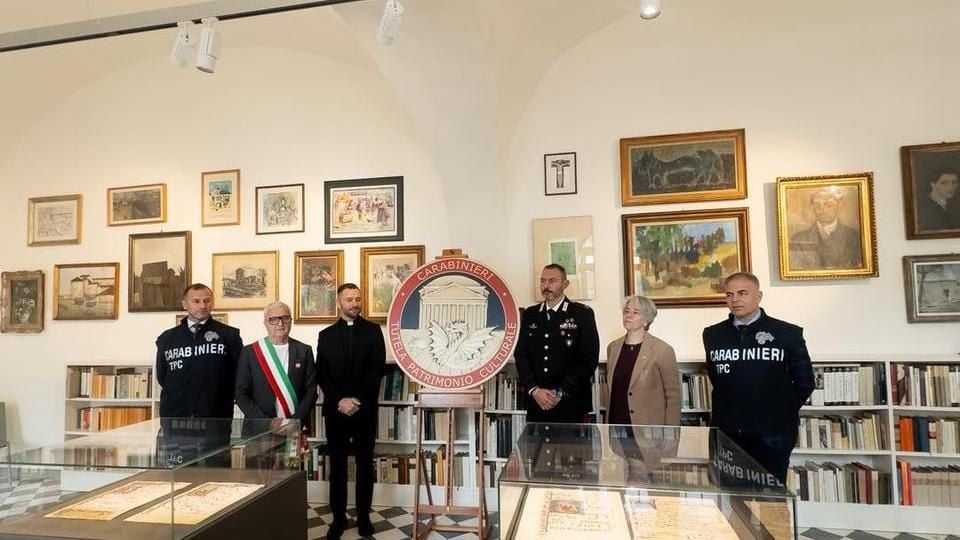 Cerimonia di restituzione di trenta pagine miniate recuperate dopo essere state rubate nel 1982. Al centro, il simbolo dei Carabinieri per la Tutela del Patrimonio Culturale; sullo sfondo, opere d’arte e libri esposti in una sala.