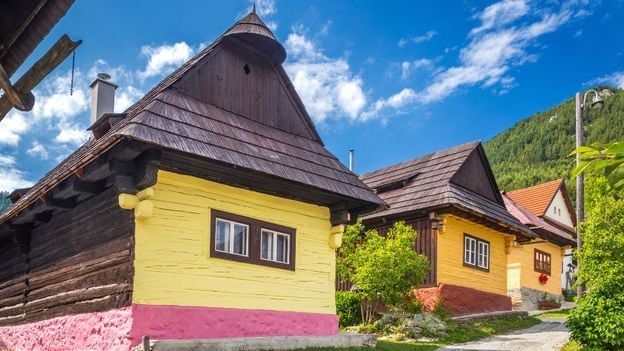 A row of traditional colorful wooden houses lining an uphill street in the small town of Vlkolínec in Slovakia.
