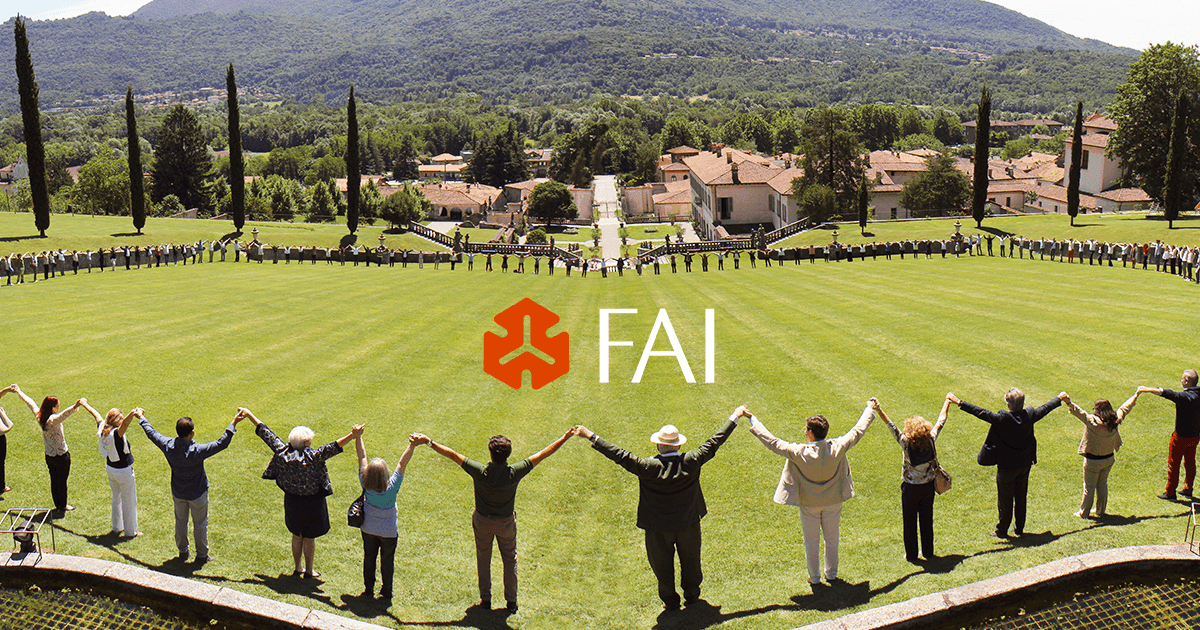 Veduta panoramica di un ampio giardino all’italiana con un gruppo di persone disposte lungo il prato e lungo i percorsi, alcune delle quali si tengono per mano. Sullo sfondo si vedono edifici storici, alberi e un paesaggio collinare. Al centro dell’immagine compare il logo del FAI.