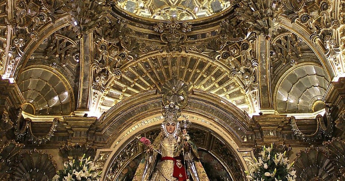 Statua della Madonna con Bambino, con corona e abiti riccamente decorati, collocata al centro di un elaborato altare barocco dorato, tra ornamenti e composizioni floreali.