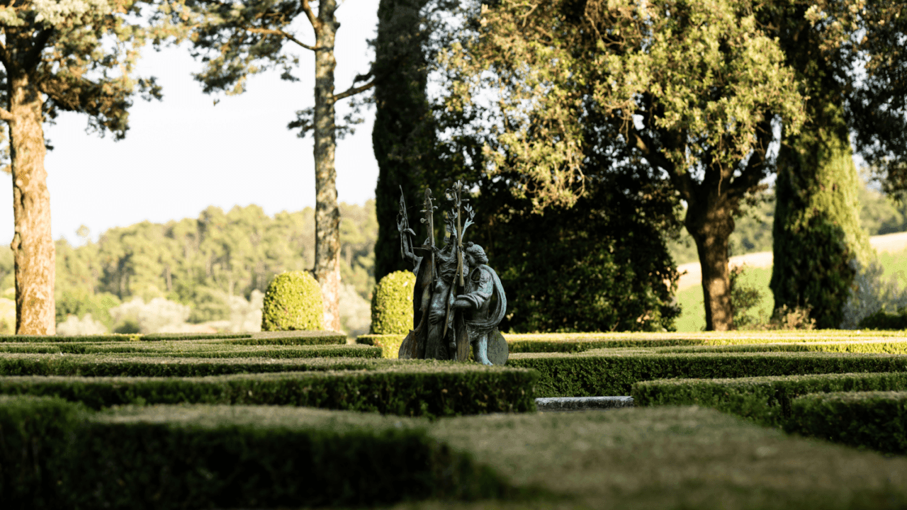 Una scultura in bronzo è collocata al centro del giardino all’italiana di Villa del Cigliano, tra siepi geometriche e alberi. Sullo sfondo si apre il paesaggio collinare del Chianti.