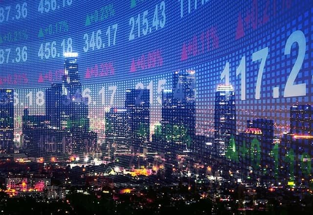 Veduta notturna di una città con grattacieli illuminati, sovrapposta a un grande tabellone digitale con quotazioni, numeri e indicatori finanziari in diversi colori.