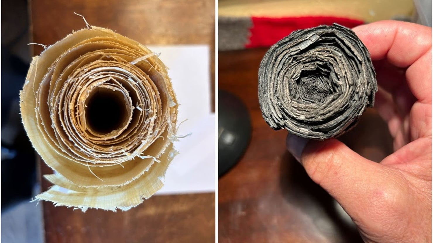 Confronto tra due rotoli visti in sezione: a sinistra un rotolo chiaro realizzato come modello sperimentale, a destra un rotolo antico annerito e deteriorato, tenuto tra le dita di una mano. In entrambi sono visibili i numerosi strati di materiale avvolti concentricamente.