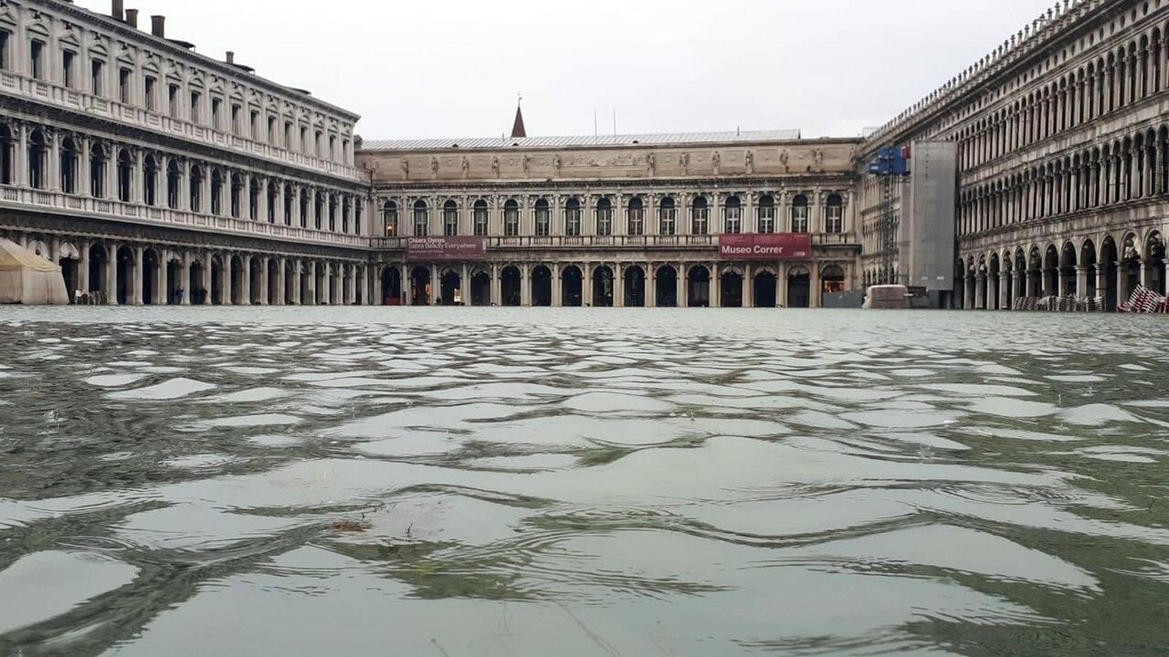 Piazza San Marco a Venezia completamente allagata dall’acqua alta. In primo piano l’acqua ricopre la pavimentazione della piazza, mentre sullo sfondo si affacciano gli edifici storici delle Procuratie.