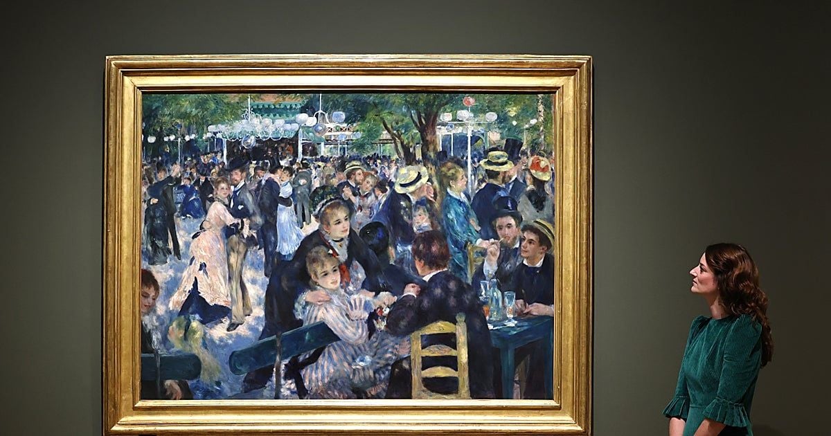 Il dipinto Bal du moulin de la Galette di Pierre-Auguste Renoir, esposto in una sala museale con cornice dorata. A destra, una visitatrice osserva l’opera, che raffigura una folla riunita all’aperto tra tavoli e danze.