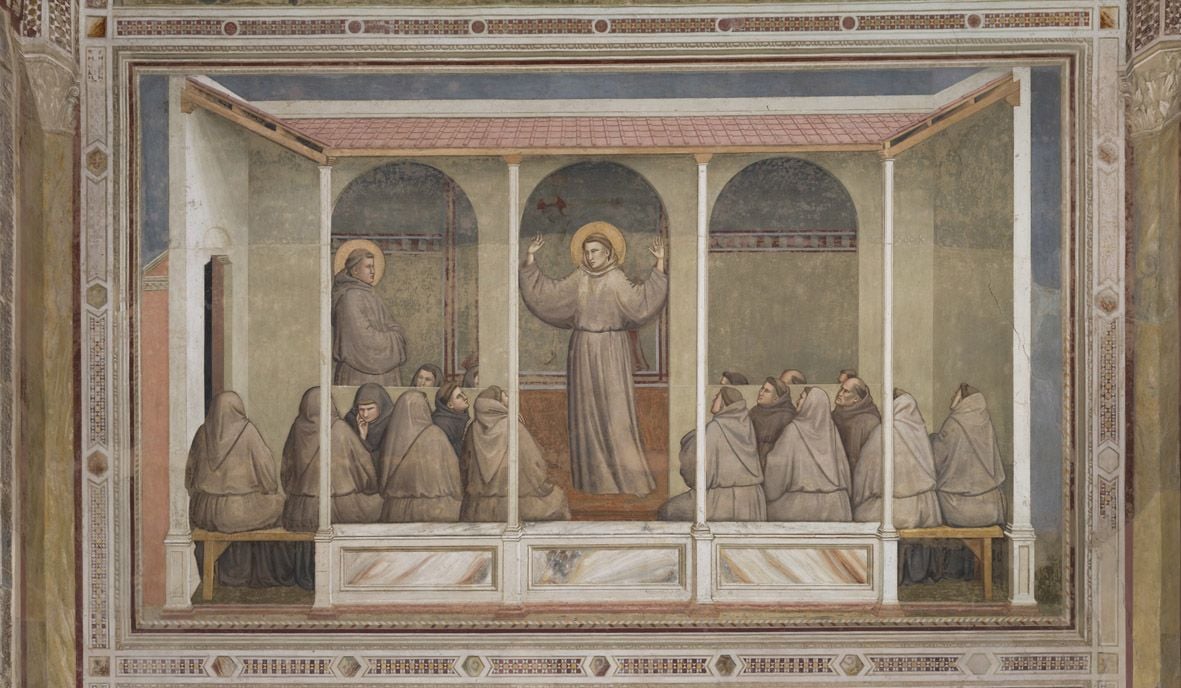 Affresco raffigurante una scena religiosa con un frate al centro, in piedi con le braccia sollevate, circondato da numerose figure vestite con abiti religiosi. La scena è ambientata sotto un portico con colonne e archi, decorato da elementi architettonici e motivi ornamentali.