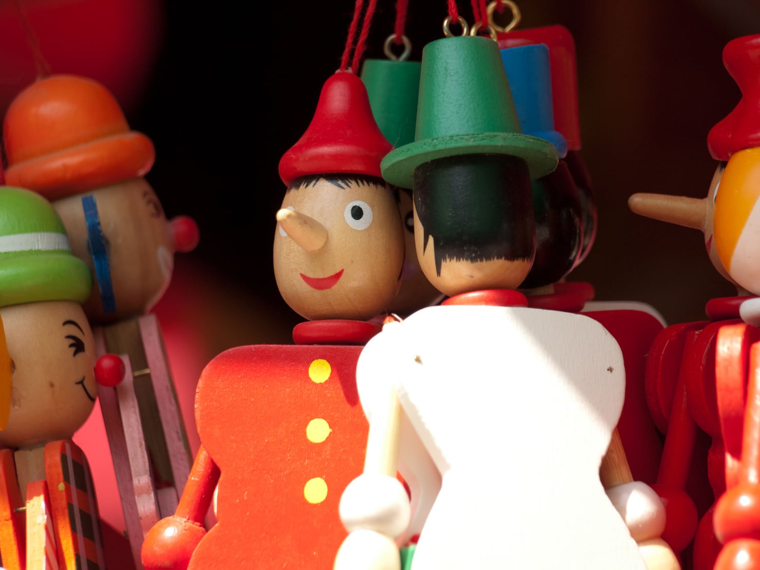 Primo piano di diverse figure di Pinocchio in legno, con nasi allungati e cappelli colorati, disposte una accanto all’altra.